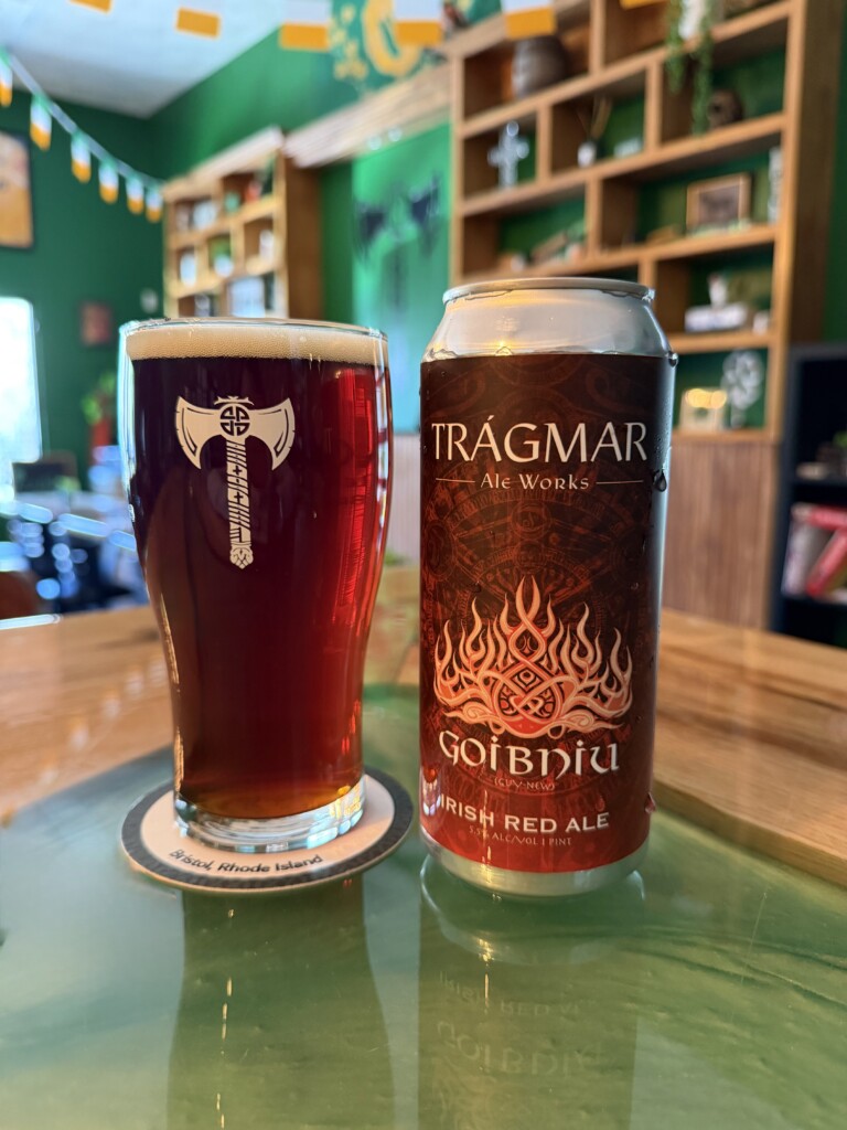 A beer can sits next to a pint of reddish liquid in a green-hued taproom.