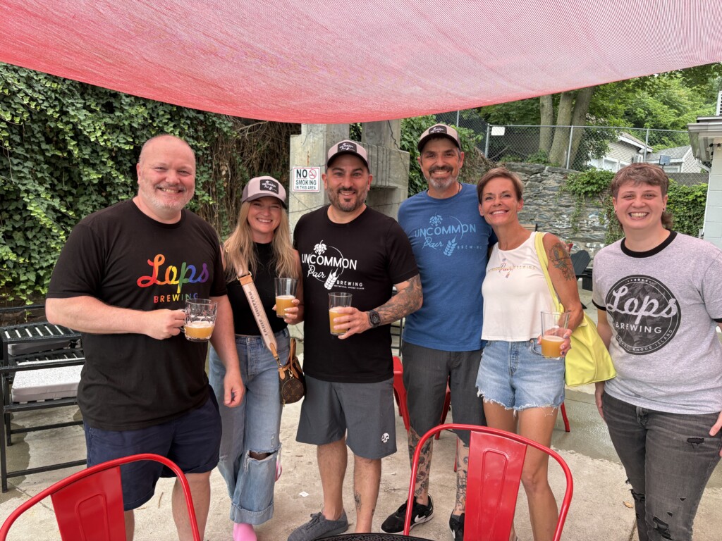 A group of people holding beers stand on an outdoor patio.