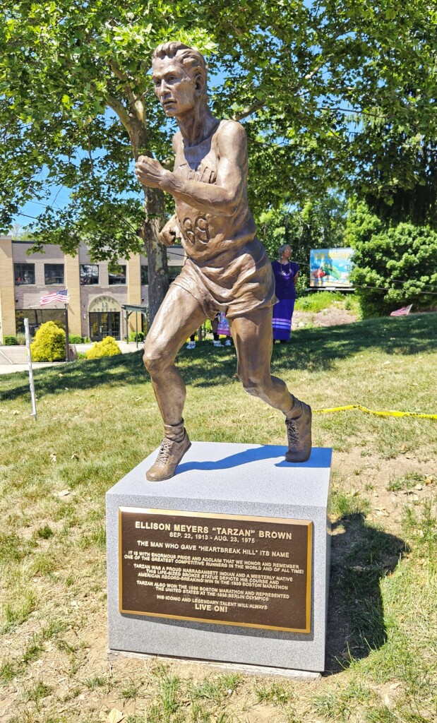 A brown statue of a man running is set against the backdrop of a park.
